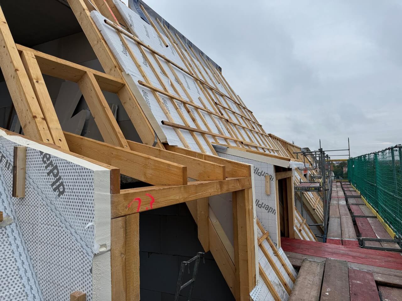 Der Dachstuhl ist errichtet, die Aufdachdämmung montiert und die Flachdächer sind vorgedeckt – nächster Schritt ist die Dämmung und Fenstermontage.