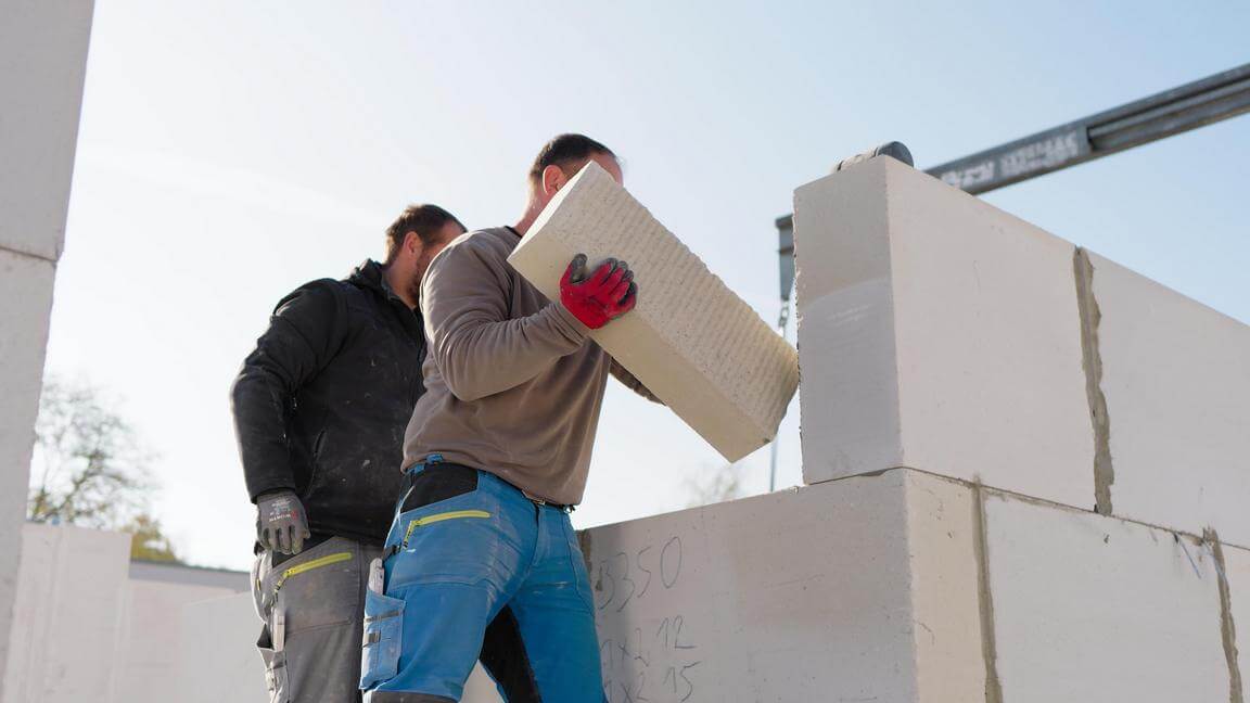 Zwei Bauarbeiter setzen präzise Gasporenbetonsteine für ein monolithisches Mauerwerk