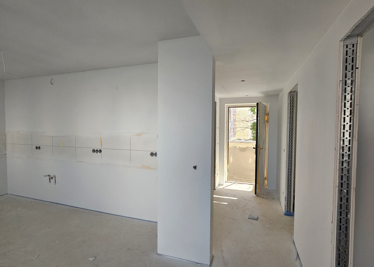 Neubauwohnung im Innenausbau mit vorbereiteten Küchenanschlüssen und Blick in einen hellen Flur mit Balkontür