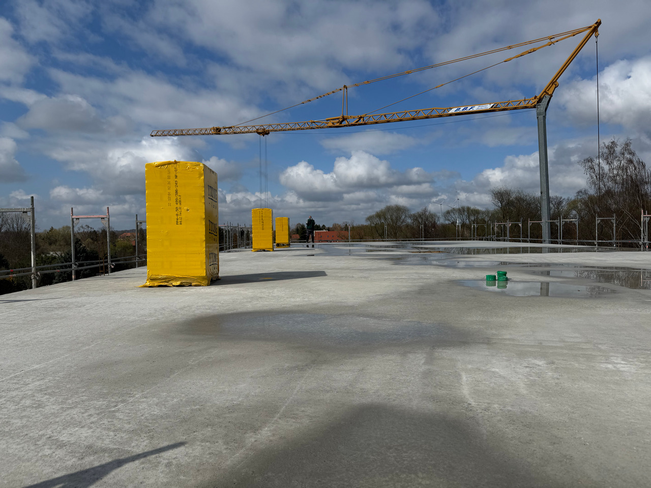 Frisch betonierte Dachgeschossdecke eines Neubaus mit Baukran und Baumaterial auf der Baustelle